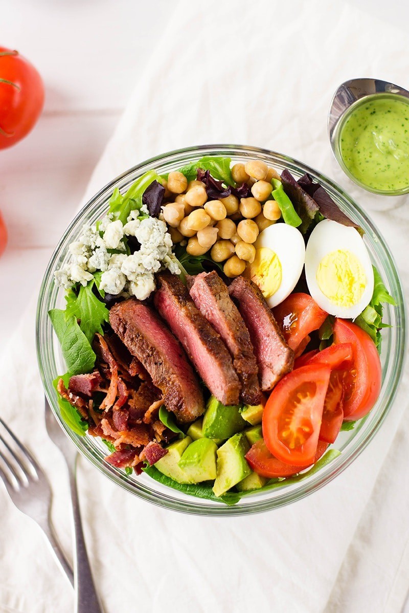 Close up of steak Cobb salad loaded with hard-boiled eggs, tomatoes, garbanzo beans, avocado, bacon strips, and crumbled Gorgonzola cheese 